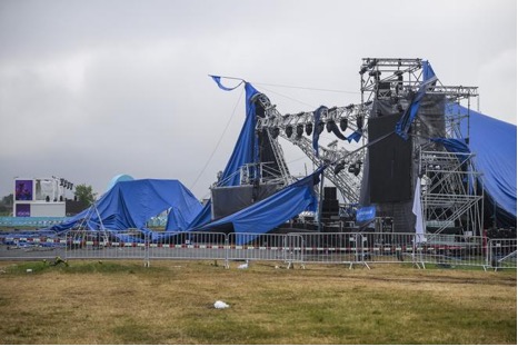 Outdoor concert stage severely damaged with torn blue tarps and bent metal frames on a cloudy day