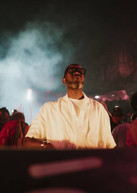 Man with glasses and a white shirt standing in a smoky, dimly lit crowd setting at night.