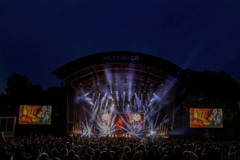 Large outdoor concert stage at night with bright spotlights and a crowd watching at the VestRock music festival.