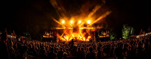 Crowd watching a nighttime concert with bright orange stage lights and smoke effects illuminating the scene.