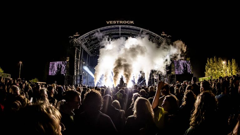 Crowd watching a nighttime concert with smoke effects on stage under a large structure labeled VESTROCK.