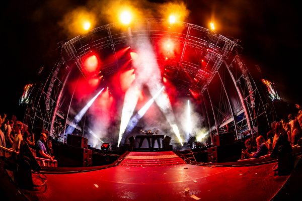 DJ performing on a large stage with bright red and white lights and smoke effects during a night concert