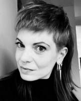 Black and white close-up portrait of a person with short hair on top and longer hair in the back, wearing earrings.