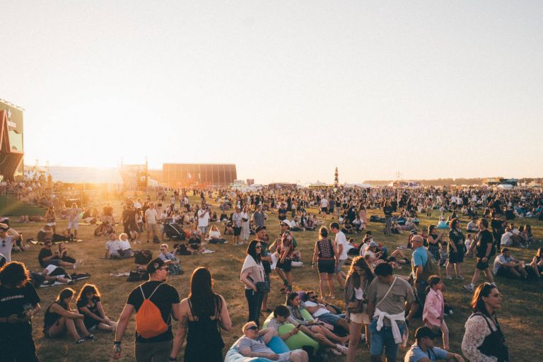 Large crowd of people socializing and relaxing on a grassy field at an outdoor festival or event during sunset