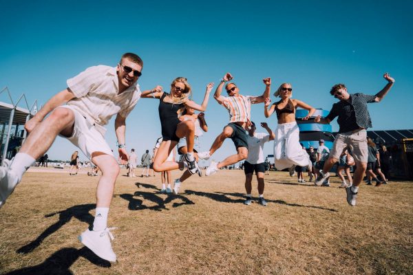Group of young people jumping and having fun outdoors on a sunny day with a clear blue sky at a festival or event.