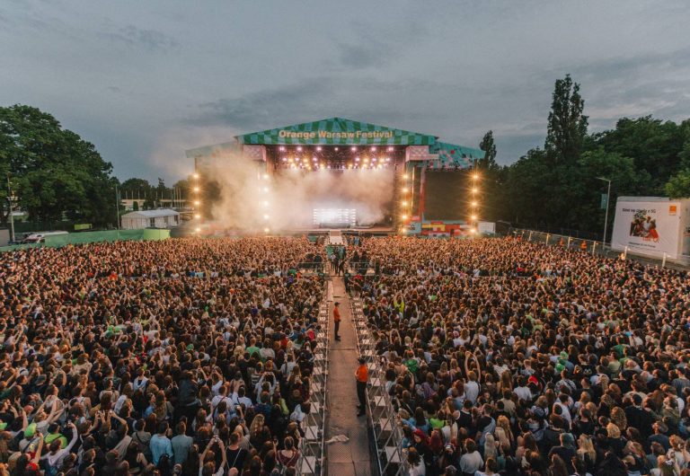 Crowded outdoor concert stage at the Orange Warsaw Festival with bright lights and smoke effects during dusk.