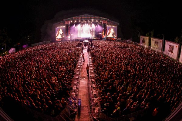 Large crowd attending a night concert at Orange Warsaw Festival with a singer performing on stage and displayed on giant screens.
