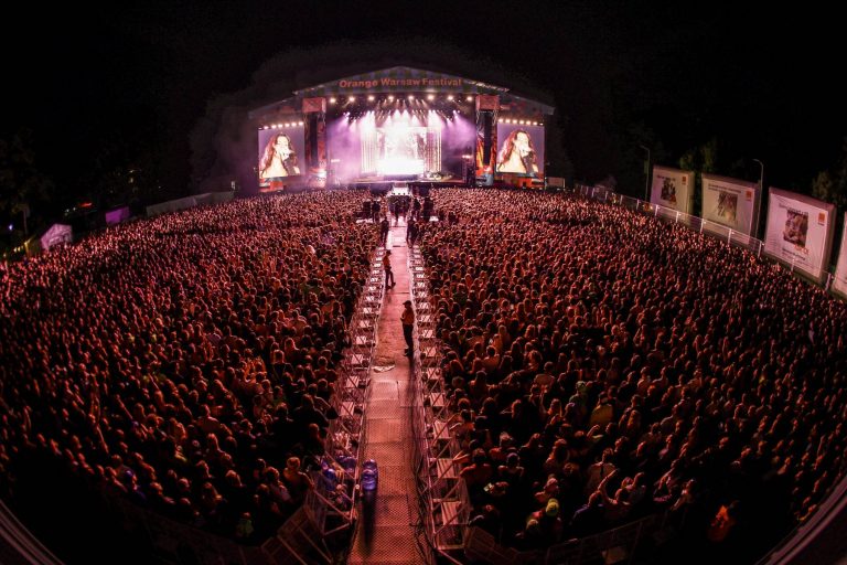 Large crowd attending a night concert at Orange Warsaw Festival with a singer performing on stage and displayed on giant screens.