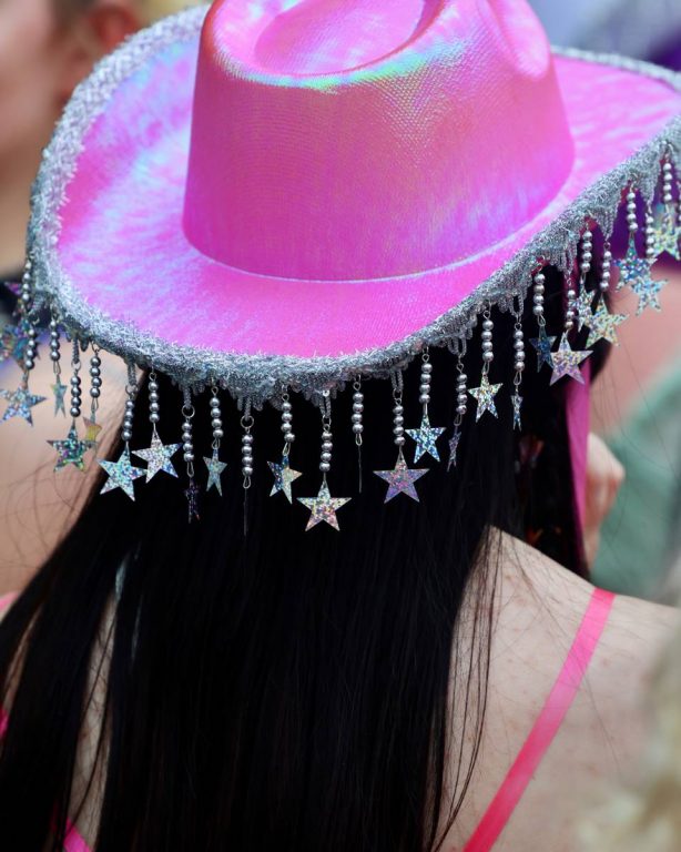 Back view of a person wearing a shiny pink cowboy hat with dangling silver star and bead decorations along the brim.