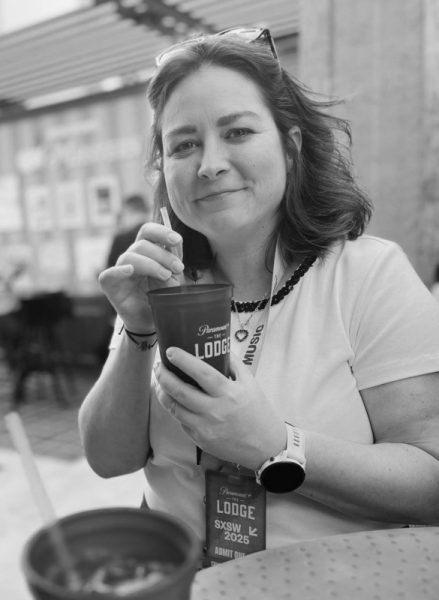 Woman smiling while holding a cup with a straw, wearing a lanyard with