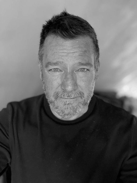 Black and white close-up portrait of a middle-aged man with short hair, light stubble, and wearing a dark sweater.