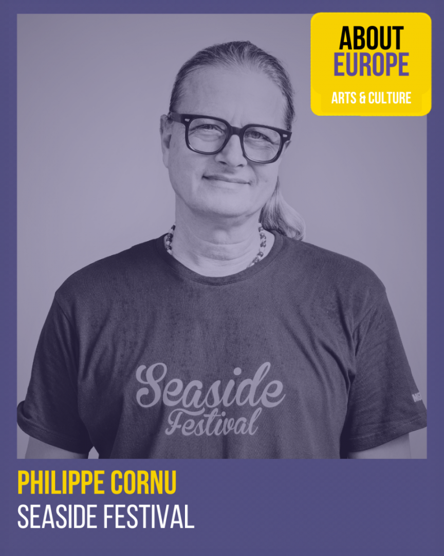 Man with glasses and long hair wearing a Seaside Festival t-shirt, identified as Philippe Cornu, with About Europe Arts & Culture branding.