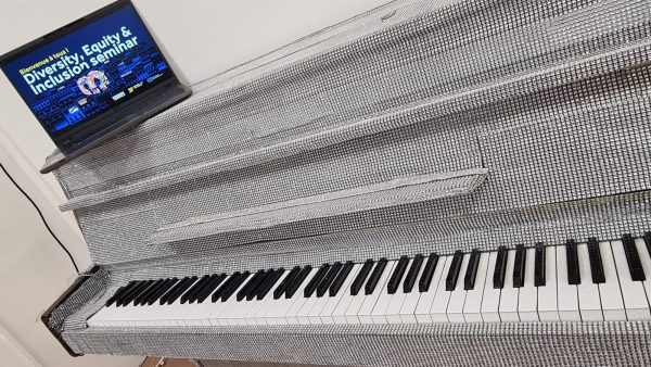 Piano wrapped in reflective silver material with a laptop on top displaying a Diversity, Equity & Inclusion seminar slide